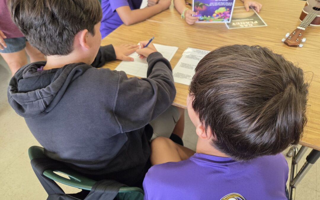 Middle-school students gathered around a desk doing an activity on paper.